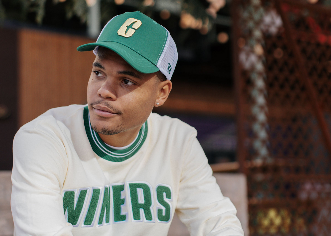 Man in a cream Niners sweater and a green Charlotte cap